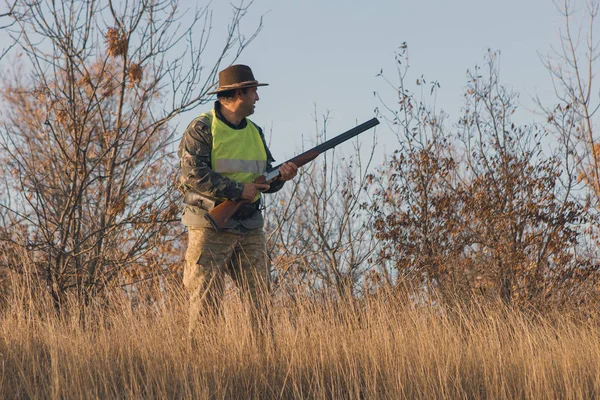 銃を持ったハンターのシルエット 迷彩の銃と草原で反射ベスト帽子のハンター — ストック写真