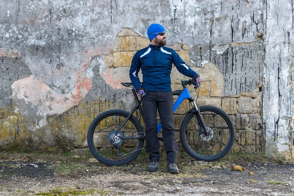 A guy in sportswear riding clothes on a modern mountain carbon bike with an air suspension fork at a vintage brick concrete wall.