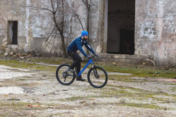 A guy in sportswear riding clothes on a modern mountain carbon bike with an air suspension fork at a vintage brick concrete wall.