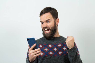 Beyaz arka planda akıllı telefon kullanan kızgın beyaz sakallı genç adam.