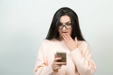 Surprised beautiful young caucasian woman wear glsses watching smartphone on white background