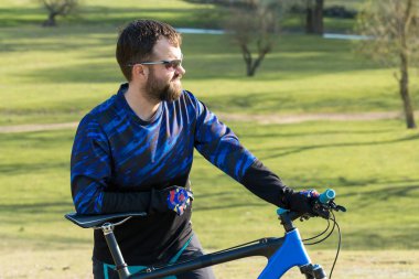 Bisikletçi şort ve mayo modern bir karbon hardtail bisiklet ile bir hava süspansiyon çatal sürmek off-road ormana yakın yeşil tepelerde