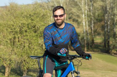 Bisikletçi şort ve mayo modern bir karbon hardtail bisiklet ile bir hava süspansiyon çatal sürmek off-road ormana yakın yeşil tepelerde