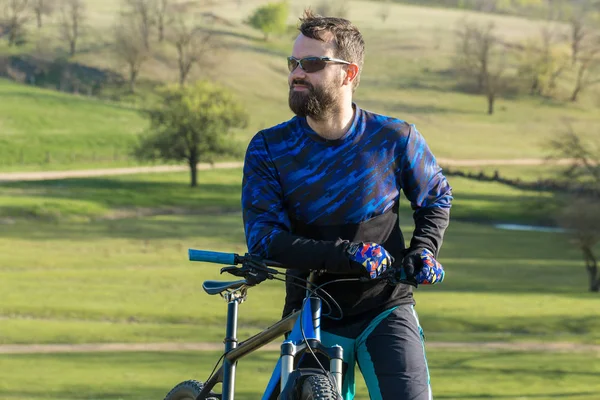 森の近くの緑の丘の上にエアサスペンションフォークを搭載したモダンなカーボンハードテールバイクのショートパンツとジャージのサイクリスト — ストック写真