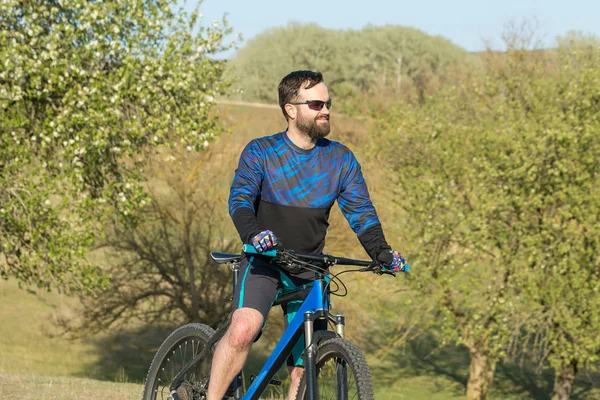 stock image Cyclist in shorts and jersey on a modern carbon hardtail bike with an air suspension fork rides off-road on green hills near the forest