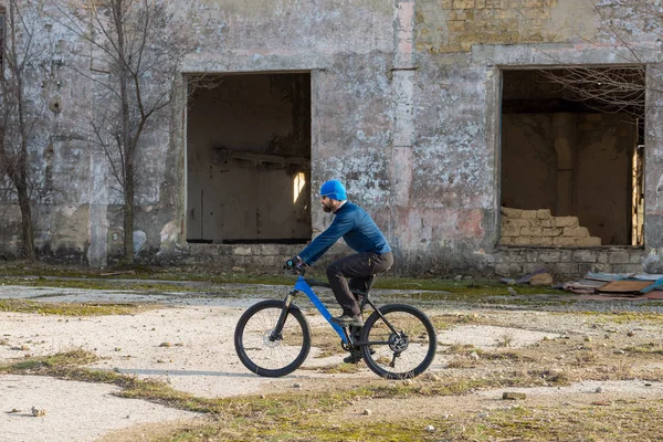 A guy in sportswear riding clothes on a modern mountain carbon bike with an air suspension fork at a vintage brick concrete wall.