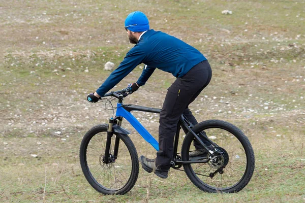 A guy in sportswear riding clothes on a modern mountain carbon bike with an air suspension fork at a vintage brick concrete wall.