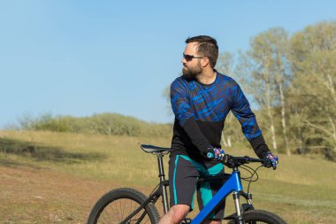 Bisikletçi şort ve mayo modern bir karbon hardtail bisiklet ile bir hava süspansiyon çatal sürmek off-road ormana yakın yeşil tepelerde