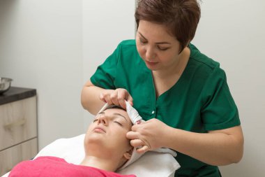 Yüz bakımı. Güzellik uzmanı güzellik salonunda fırça kullanarak yüzüne güzellik maskesi takıyor.