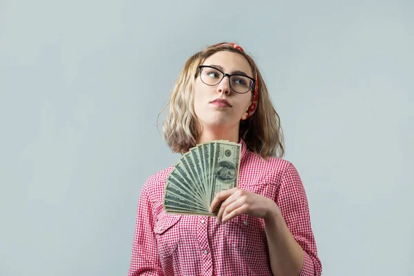 灰色の背景の上に米ドルのお金を持つメガネの赤いチェックのシャツを着た若い美しい女性のクローズアップ — ストック写真