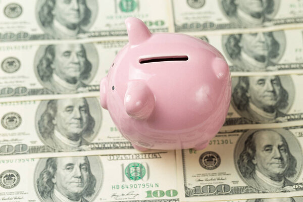 Свиная копилка на фоне 100 долларовых купюр и физических монет биткойнов. Концепция богатства и обмена.