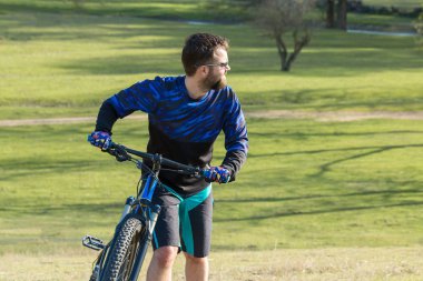 Taze yeşil yaz ormanının arka planına karşı bir uçurumun üzerinde duran bir hava süspansiyon çatal ile modern bir karbon hardtail bisiklet üzerinde şort ve mayo Bisikletçi