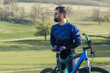 Taze yeşil yaz ormanının arka planına karşı bir uçurumun üzerinde duran bir hava süspansiyon çatal ile modern bir karbon hardtail bisiklet üzerinde şort ve mayo Bisikletçi