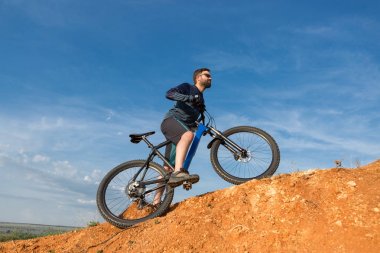 Şort ve mayo modern bir karbon hardtail bisiklet üzerinde bir hava süspansiyon çatal sürmek off-road turuncu-kırmızı tepelerde yaz aylarında gün batımı akşamı