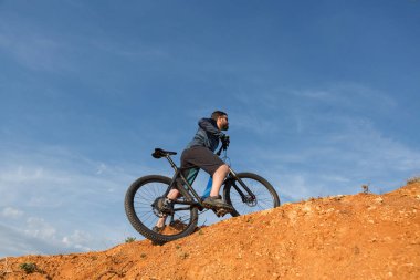 Şort ve mayo modern bir karbon hardtail bisiklet üzerinde bir hava süspansiyon çatal sürmek off-road turuncu-kırmızı tepelerde yaz aylarında gün batımı akşamı