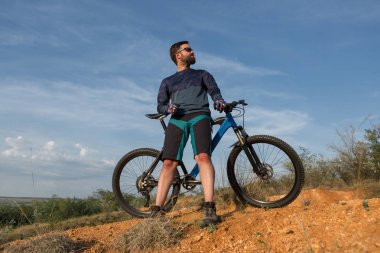 Şort ve mayo modern bir karbon hardtail bisiklet üzerinde bir hava süspansiyon çatal sürmek off-road turuncu-kırmızı tepelerde yaz aylarında gün batımı akşamı
