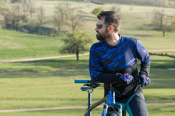 Cyclist in shorts and jersey on a modern carbon hardtail bike with an air suspension fork standing on a cliff against the background of fresh green summer forest