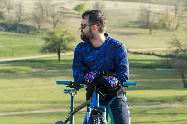 Cyclist in shorts and jersey on a modern carbon hardtail bike with an air suspension fork standing on a cliff against the background of fresh green summer forest