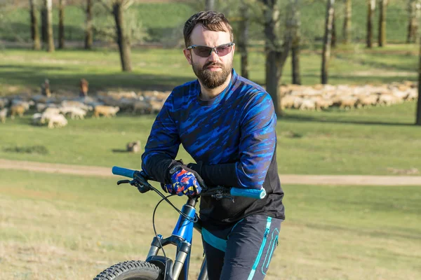 Cyclist in shorts and jersey on a modern carbon hardtail bike with an air suspension fork standing on a cliff against the background of fresh green summer forest