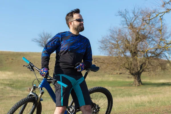 Cyclist in shorts and jersey on a modern carbon hardtail bike with an air suspension fork standing on a cliff against the background of fresh green summer forest