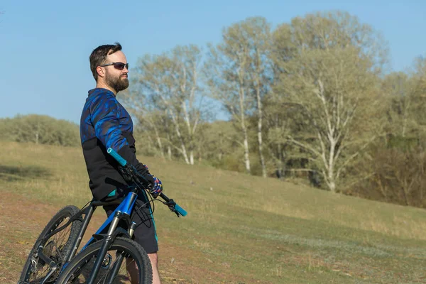 Cyclist in shorts and jersey on a modern carbon hardtail bike with an air suspension fork standing on a cliff against the background of fresh green summer forest