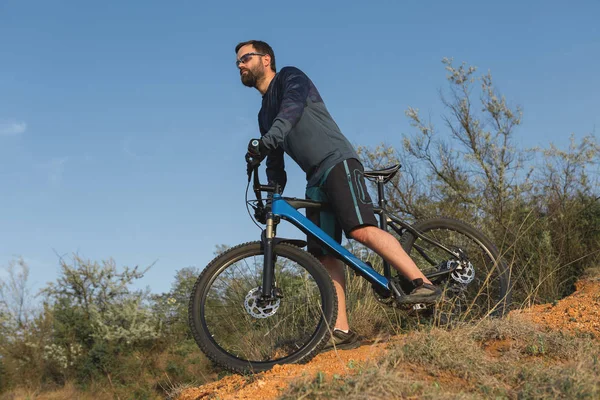 Cyclist in shorts and jersey on a modern carbon hardtail bike with an air suspension fork rides off-road on the orange-red hills at sunset evening in summer