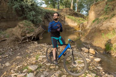 Şort ve mayo modern bir karbon hardtail bisiklet üzerinde bir hava süspansiyon çatal sürmek off-road turuncu-kırmızı tepelerde yaz aylarında gün batımı akşamı