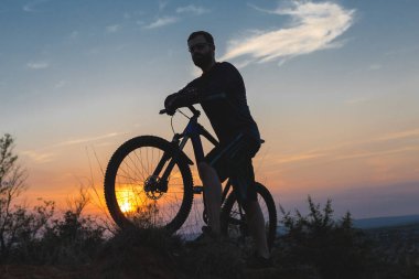 Şort ve mayo modern bir karbon hardtail bisiklet üzerinde bir hava süspansiyon çatal sürmek off-road turuncu-kırmızı tepelerde yaz aylarında gün batımı akşamı