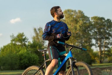 Şort ve mayo modern bir karbon hardtail bisiklet üzerinde bir hava süspansiyon çatal sürmek off-road turuncu-kırmızı tepelerde yaz aylarında gün batımı akşamı