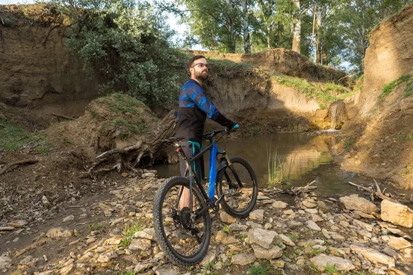 Cyclist in shorts and jersey on a modern carbon hardtail bike with an air suspension fork rides off-road on the orange-red hills at sunset evening in summer