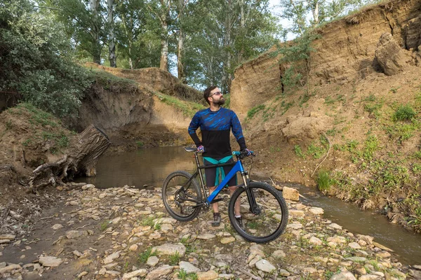 Cyclist in shorts and jersey on a modern carbon hardtail bike with an air suspension fork rides off-road on the orange-red hills at sunset evening in summer