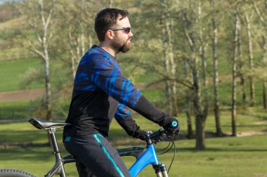 Taze yeşil yaz ormanının arka planına karşı bir uçurumun üzerinde duran bir hava süspansiyon çatal ile modern bir karbon hardtail bisiklet üzerinde şort ve mayo Bisikletçi