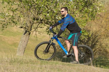 Taze yeşil yaz ormanının arka planına karşı bir uçurumun üzerinde duran bir hava süspansiyon çatal ile modern bir karbon hardtail bisiklet üzerinde şort ve mayo Bisikletçi