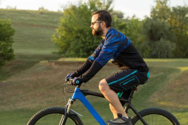 Taze yeşil yaz ormanının arka planına karşı bir uçurumun üzerinde duran bir hava süspansiyon çatal ile modern bir karbon hardtail bisiklet üzerinde şort ve mayo Bisikletçi