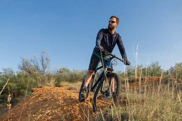 Cyclist in shorts and jersey on a modern carbon hardtail bike with an air suspension fork standing on a cliff against the background of fresh green summer forest