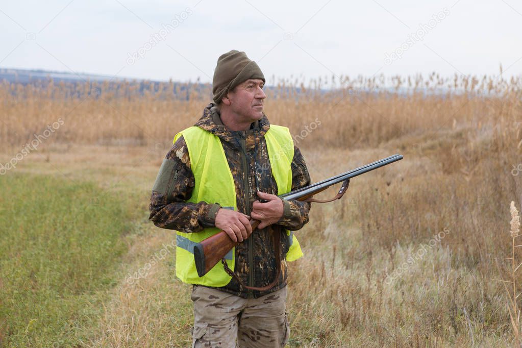 Hunting period, autumn season open. A hunter with a gun in his hands in hunting clothes in the autumn forest in search of a trophy.