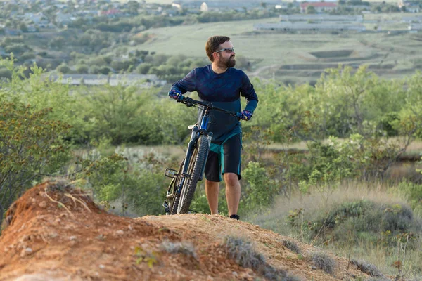 Cyclist in shorts and jersey on a modern carbon hardtail bike with an air suspension fork rides off-road on the orange-red hills at sunset evening in summer