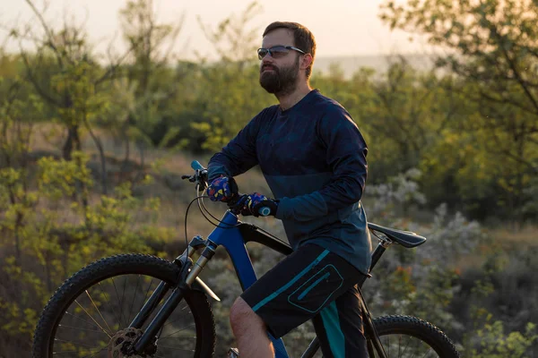 Cyclist in shorts and jersey on a modern carbon hardtail bike with an air suspension fork rides off-road on the orange-red hills at sunset evening in summer