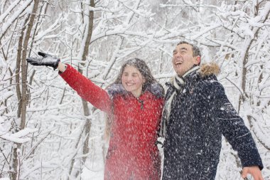 Adam ve kız kış ormanlarında dinleniyorlar. Karda karı-koca. Genç bir çift kış parkında yürüyor.