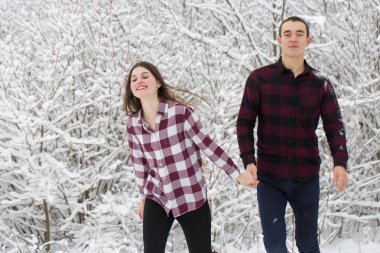 Adam ve kız kış ormanlarında dinleniyorlar. Karda karı-koca. Genç bir çift kış parkında yürüyor.