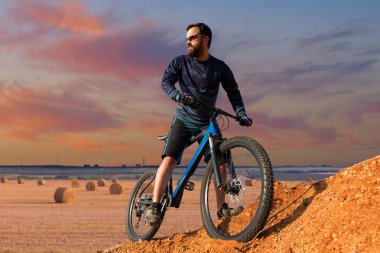 Şort ve mayo modern bir karbon hardtail bisiklet üzerinde bir hava süspansiyon çatal sürmek off-road turuncu-kırmızı tepelerde yaz aylarında gün batımı akşamı