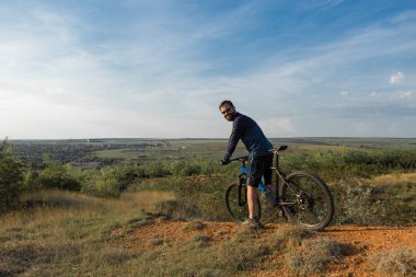 Şort ve mayo modern bir karbon hardtail bisiklet üzerinde bir hava süspansiyon çatal sürmek off-road turuncu-kırmızı tepelerde yaz aylarında gün batımı akşamı