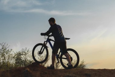 Şort ve mayo modern bir karbon hardtail bisiklet üzerinde bir hava süspansiyon çatal sürmek off-road turuncu-kırmızı tepelerde yaz aylarında gün batımı akşamı