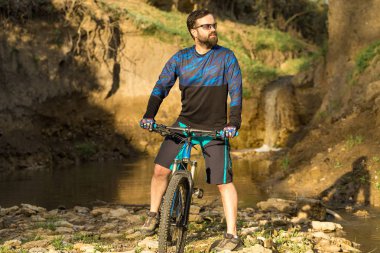 Şort ve mayo modern bir karbon hardtail bisiklet üzerinde bir hava süspansiyon çatal sürmek off-road turuncu-kırmızı tepelerde yaz aylarında gün batımı akşamı