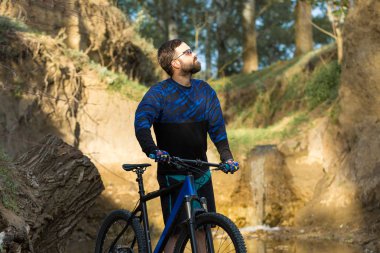 Şort ve mayo modern bir karbon hardtail bisiklet üzerinde bir hava süspansiyon çatal sürmek off-road turuncu-kırmızı tepelerde yaz aylarında gün batımı akşamı