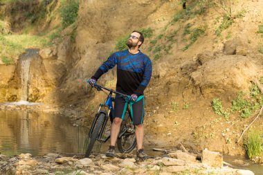 Şort ve mayo modern bir karbon hardtail bisiklet üzerinde bir hava süspansiyon çatal sürmek off-road turuncu-kırmızı tepelerde yaz aylarında gün batımı akşamı