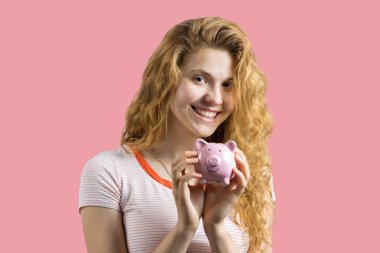 Beyaz arka plan üzerinde genç kırmızı saçlı kıvırcık kız kumbara tutan ve gesturing sevinir. Nakit yatırımlar ve sigorta güvenilirlik kavramı. Kız kumbara fiziksel Bitcoin koyar