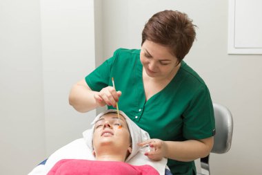 Yüz bakımı. Güzellik uzmanı güzellik salonunda fırça kullanarak yüzüne güzellik maskesi takıyor.