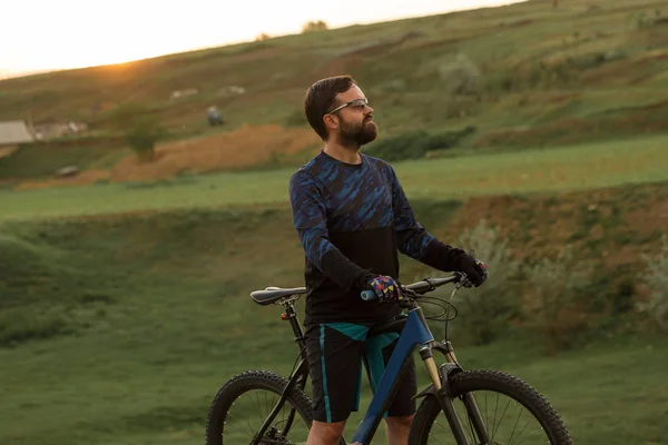 Cyclist in shorts and jersey on a modern carbon hardtail bike with an air suspension fork rides off-road on the orange-red hills at sunset evening in summer