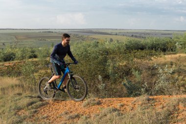 Şort ve mayo modern bir karbon hardtail bisiklet üzerinde bir hava süspansiyon çatal sürmek off-road turuncu-kırmızı tepelerde yaz aylarında gün batımı akşamı